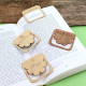 Quatre accroche-pages en bois posés sur un livre ouvert, marquage visible sur trois pièces.