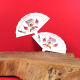 Deux éventails en papier blanc imprimé posés sur une surface en bois avec fond rouge, impressions colorées visibles sur chaque f