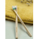 Deux brosses à dents en bois clair personnalisables disposées en croix sur une serviette textile jaune