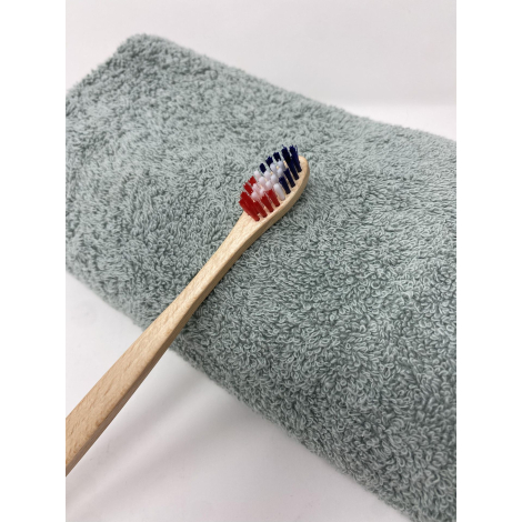 Brosse à dents en bois clair posée sur une serviette textile vert clair, sans marquage visible