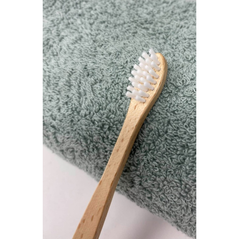 Brosse à dents pour enfant en bois clair présentée sur serviette textile vert clair, vue horizontale avec tête étroite et poils 