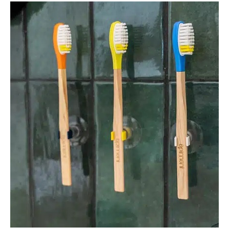 Trois brosses à dents disposées verticalement contre un mur carrelé foncé, chacune avec un manche en bois clair et une tête colo