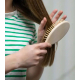 Brosse à cheveux tenue à la main et utilisée sur des cheveux, montrant le dos lisse de la tête et le manche en bois clair. Les p