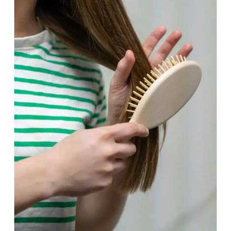 Brosse à cheveux tenue à la main et utilisée sur des cheveux, montrant le dos lisse de la tête et le manche en bois clair. Les p