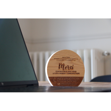 Trophée en bois clair de forme semi-circulaire, photographié en situation à côté d’un écran, personnalisation apparente sur la f