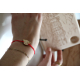 Bracelet en bois porté au poignet, médaillon en bois gravé en forme de tête d’ours avec cordon rouge, montré en situation avec a