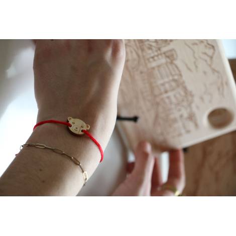 Bracelet en bois porté au poignet, médaillon en bois gravé en forme de tête d’ours avec cordon rouge, montré en situation avec a