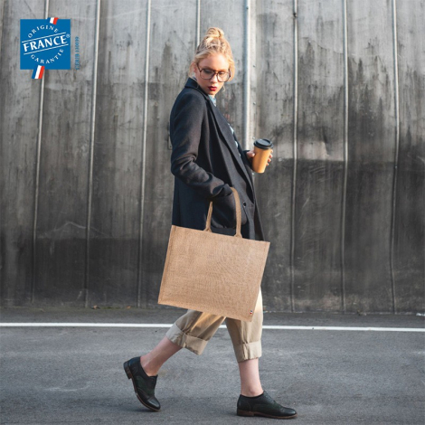 Sac en toile de jute porté à l’épaule en extérieur, vu de profil. Produit sans marquage visible.