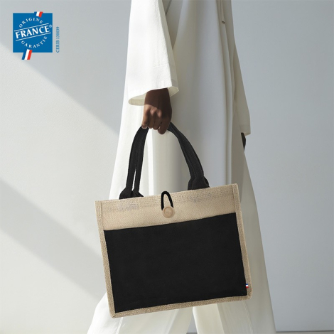 Sac en toile de jute avec bande noire porté à la main en situation. Sans personnalisation visible.