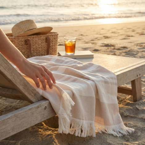 Fouta beige et blanche à rayures posée sur transat en bois sur la plage