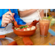 Personne utilisant une fourchette orange avec un récipient réutilisable assorti rempli d’un repas, posé sur une table à côté de 