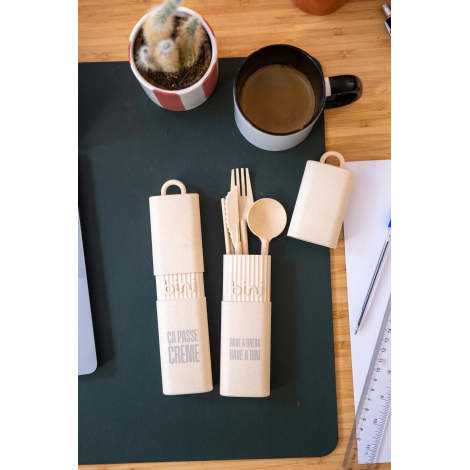 Vue de dessus de trois étuis à couverts réutilisables beige moucheté sur un bureau, dont un ouvert avec cuillère, fourchette et 