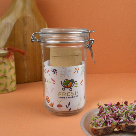 Bocal en verre personnalisé avec fermeture mécanique et sachet de graines, présenté dans une ambiance culinaire avec tartines de