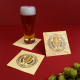 Sous-bocks carrés en bois personnalisés autour d’un verre de bière, présentés avec des fleurs de houblon sur fond rouge.