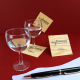 Sous-bocks carrés en bois personnalisés disposés avec deux verres à pied et un stylo sur fond rouge.