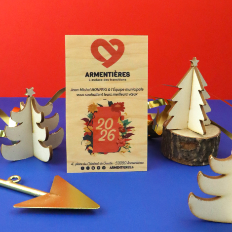 Carte de vœux en bois personnalisée en couleur, mise en scène avec des décorations de Noël sur fond rouge et bleu.