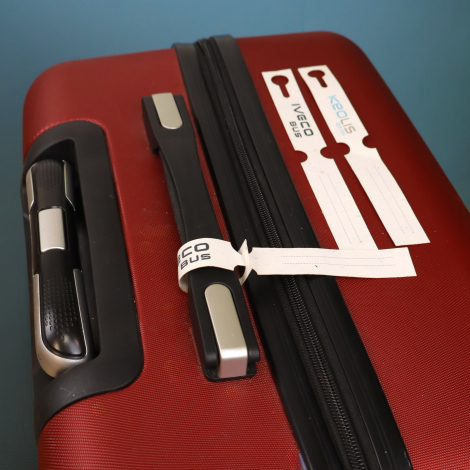 Étiquettes de bagage personnalisées blanches fixées à la poignée d’une valise rouge.