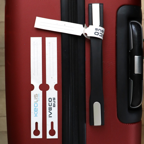 Étiquettes de bagage personnalisées avec logo et zone d’identification, présentées sur une valise rouge.