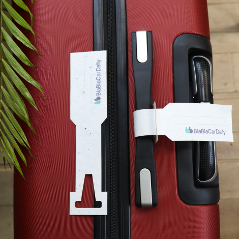 Étiquettes à bagage en papier ensemencé personnalisées avec logo, présentées sur une valise rouge.