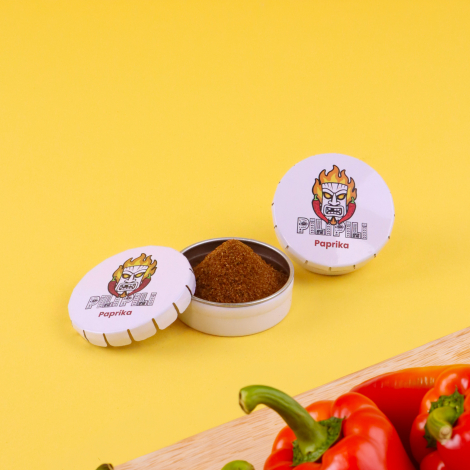 Boîtes rondes métalliques personnalisées pour épices, présentées avec herbes aromatiques et piment sur fond vert.