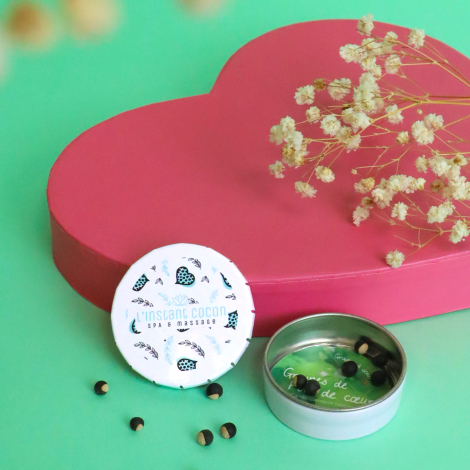 Boîte ronde métallique personnalisée avec graines de pois de cœur, mise en scène devant une boîte en forme de cœur rose sur fond