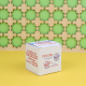 Boîte cube personnalisée en carton ensemencé avec impression publicitaire sur plusieurs faces, présentée sur fond jaune et décor