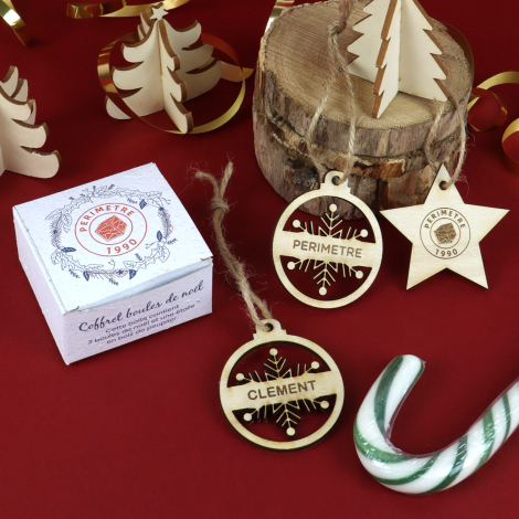 Décorations de Noël personnalisées en bois, en forme de boules et d’étoile, présentées avec leur coffret sur un décor festif rou