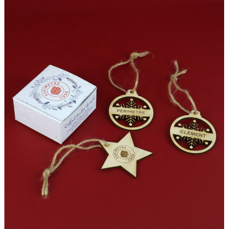 Coffret personnalisé et trois décorations de Noël en bois avec ficelle naturelle, présentés sur fond rouge.