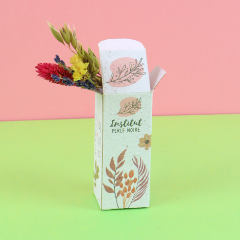 Étui personnalisé en papier à semer ouvert laissant apparaître un bouquet de fleurs séchées, sur fond rose et vert.